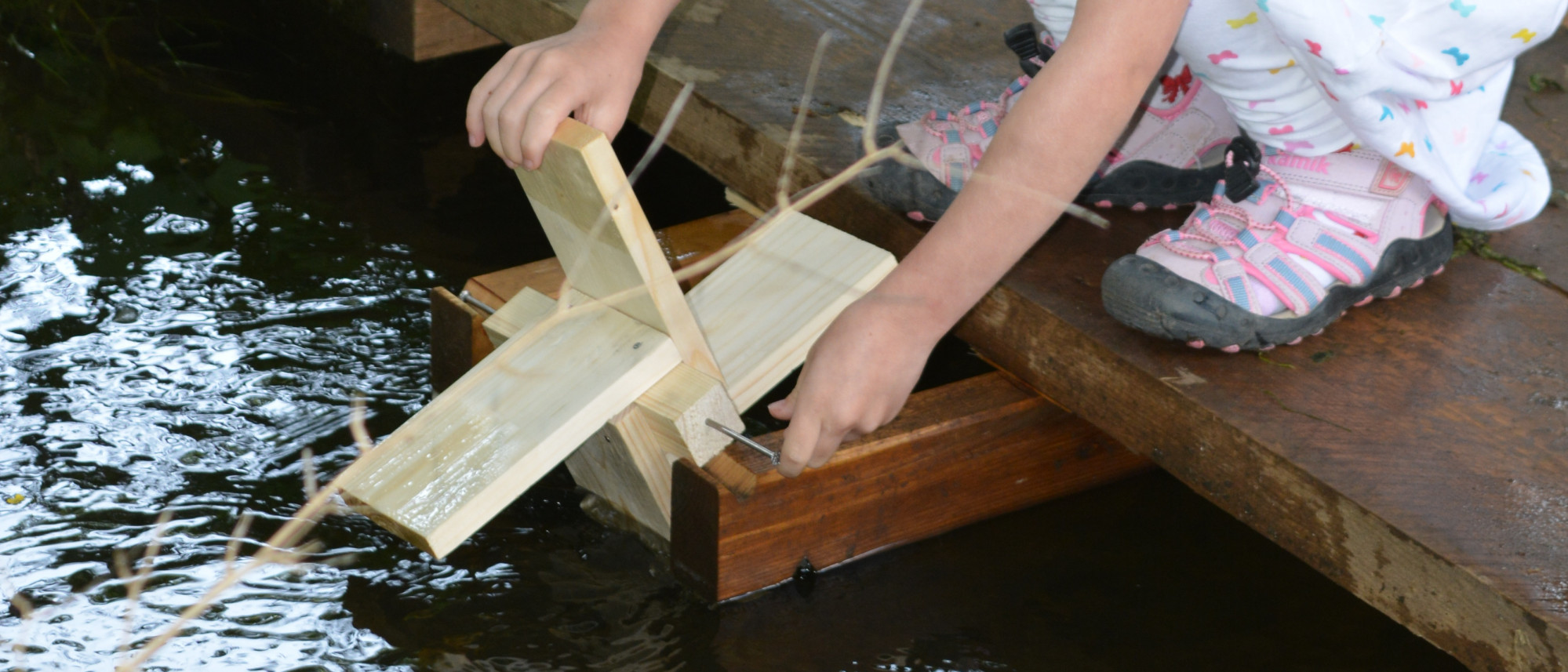 Kind probiert Holz-Wasserrad an Wasserlauf 