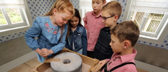Fünf Kinder an einer Handdrehmühle