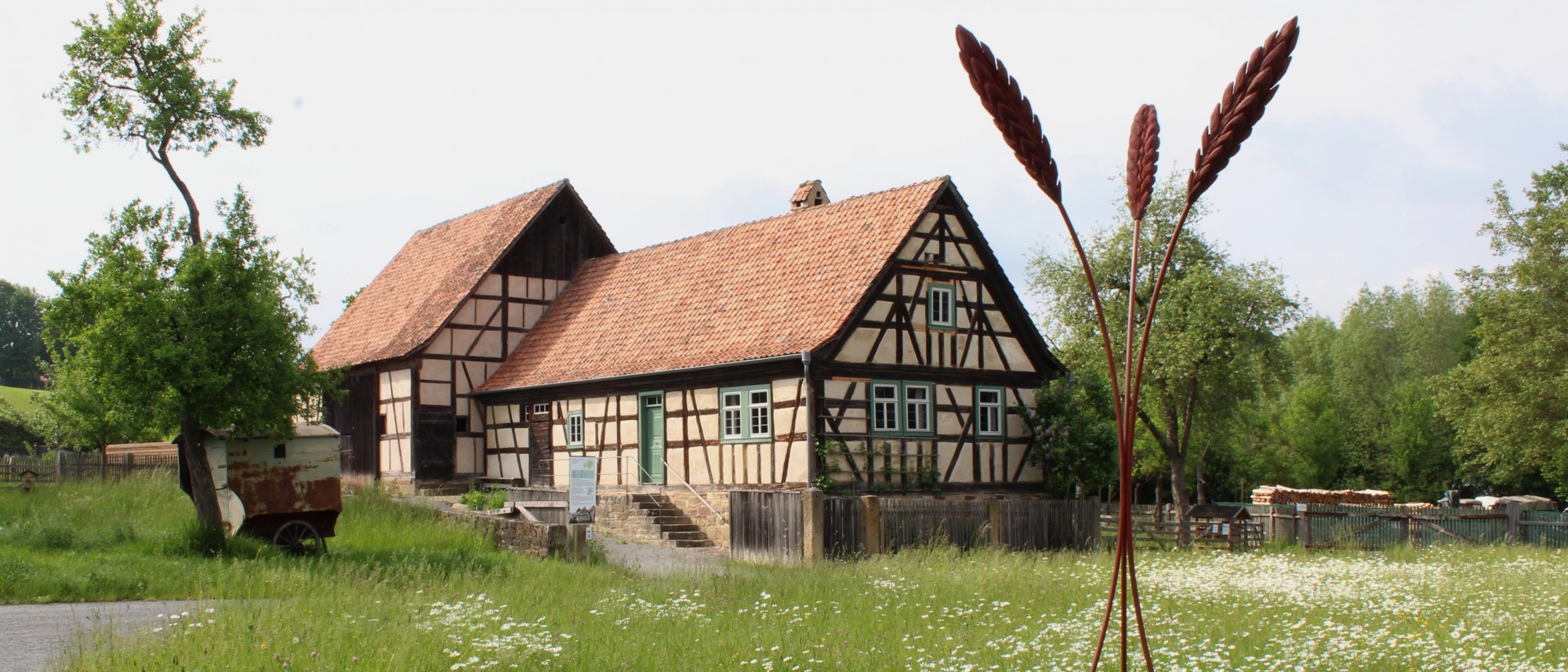 Meterhohe Skulptur in Form von drei Ähren vor Fachwerkensemble