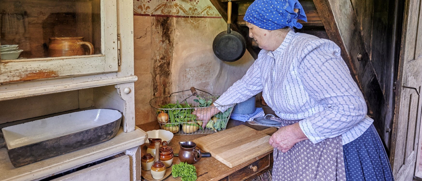 Frau in historischer Kleidung bereitet Essen in einer Küche zu