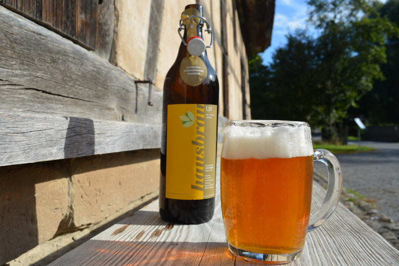 Bierflasche neben gef&uuml;lltem Bierglas auf einer Holzbank vor Fachwerkhaus
