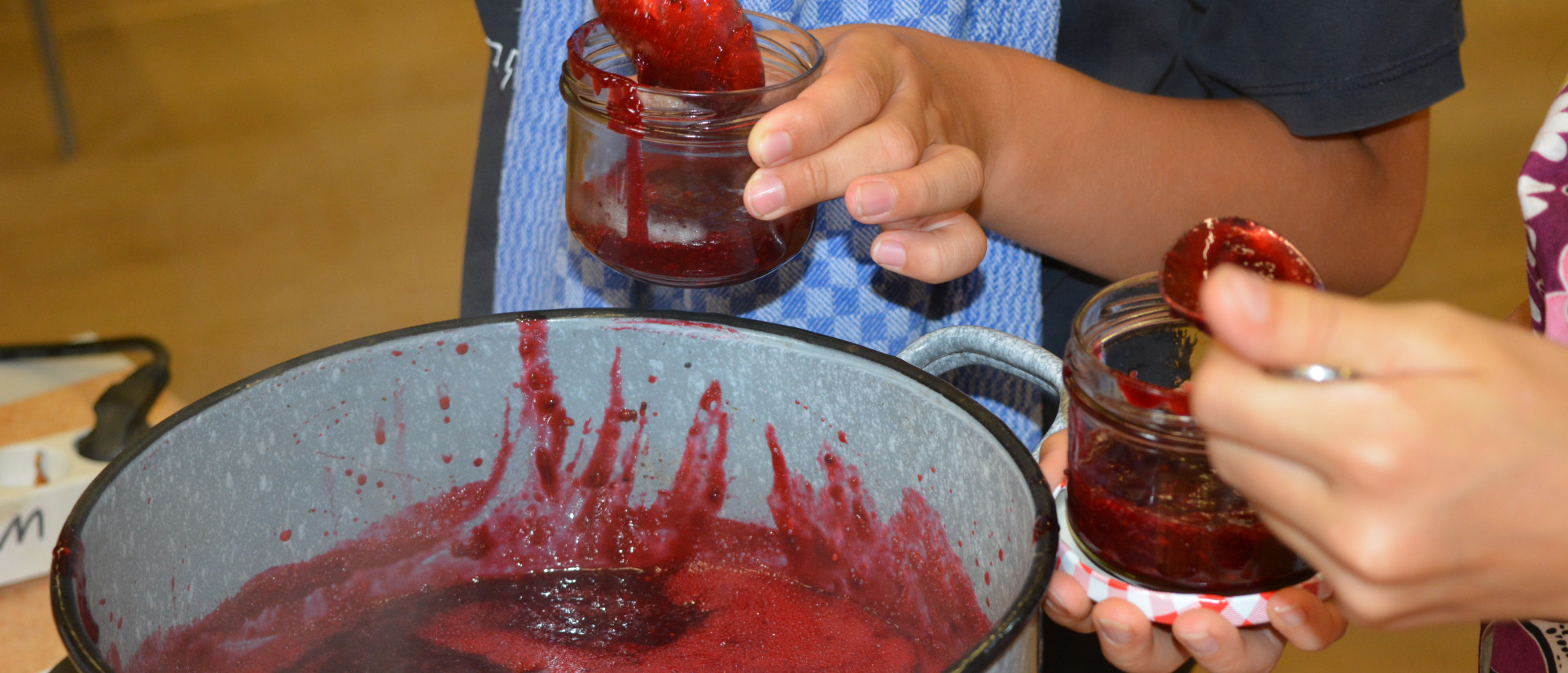 Topf mit roter Marmelade und Kinder darum stehend.