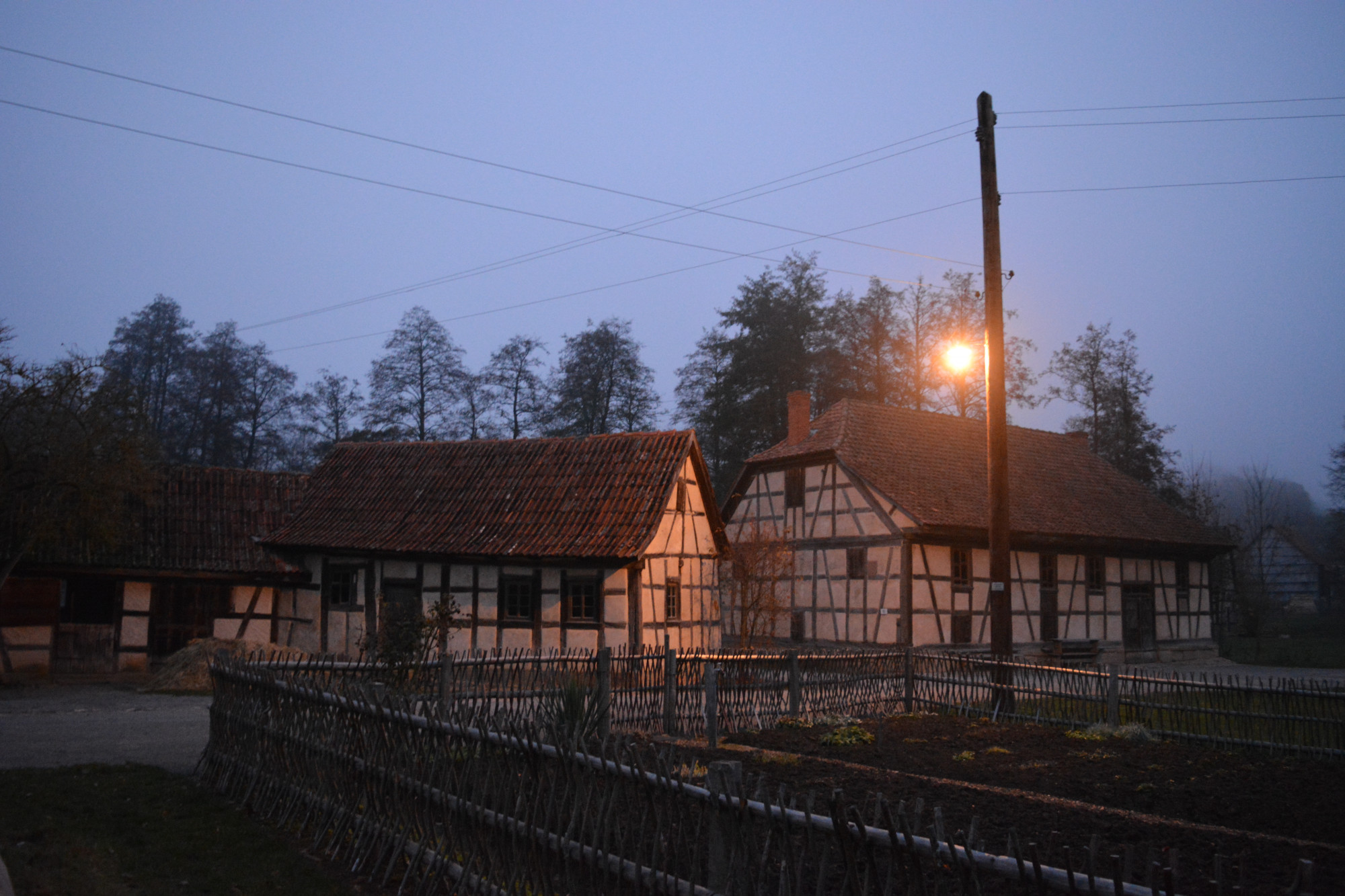 Fachwerkgeb&auml;ude bei D&auml;mmerung bei eingeschalteter Stra&szlig;enlaterne, im Vordergrund Gartenzaun