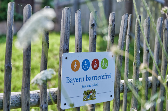 Hinweisschild Signet &quot;Bayern barrierefrei&quot; an Gartenzaun