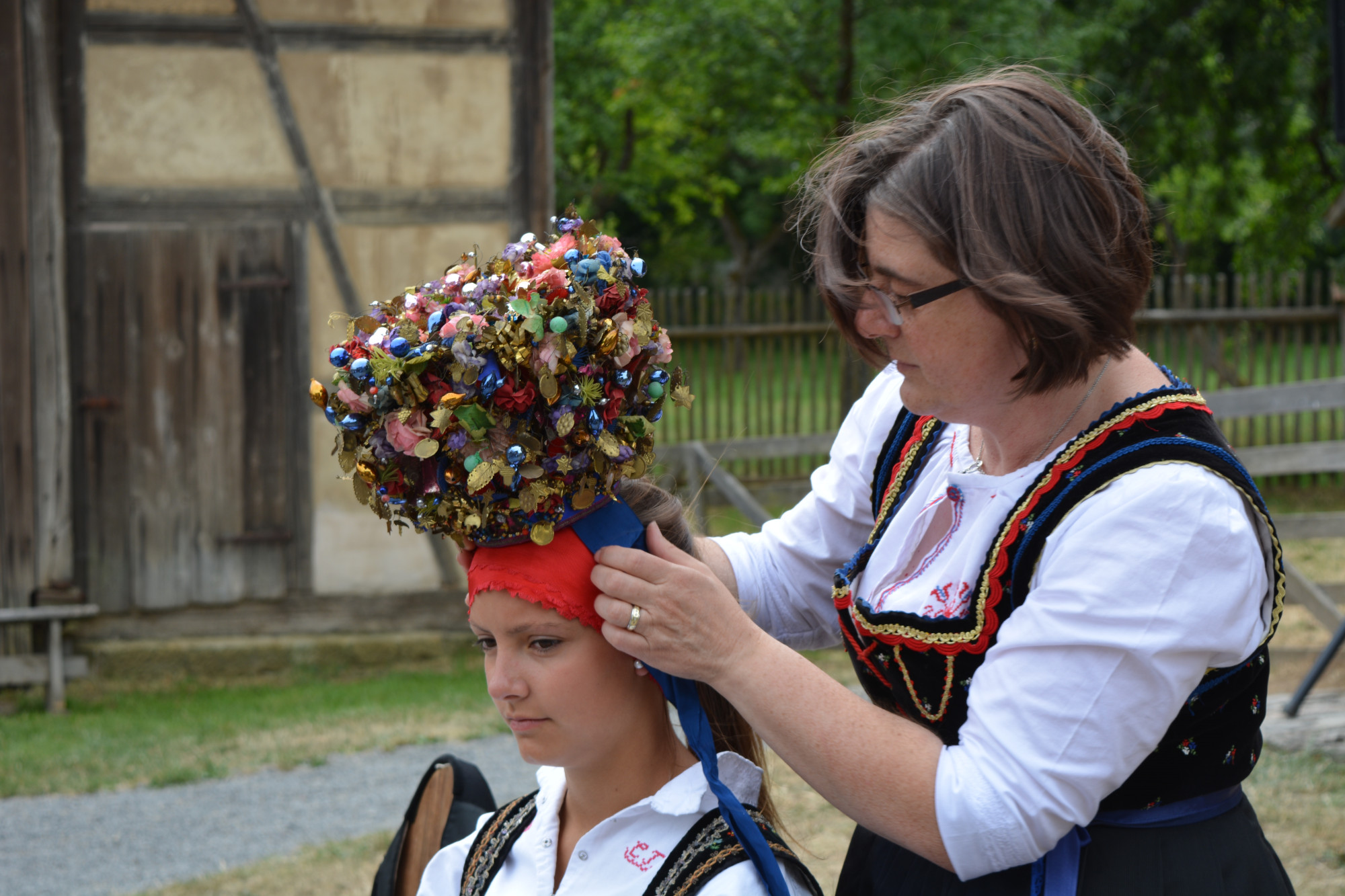 Frau in Tracht platziert eine Brautkrone auf dem Kopf einer anderen Frau