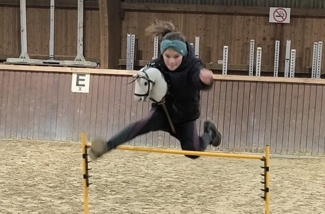 M&auml;dchen springt mit Hobby Horse &uuml;ber ein Hindernis