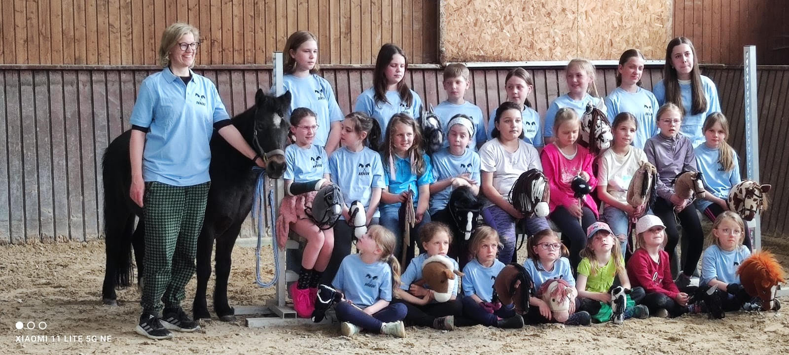 Gruppenfoto von M&auml;dchen mit Steckenpferden, daneben eine Frau mit Pony