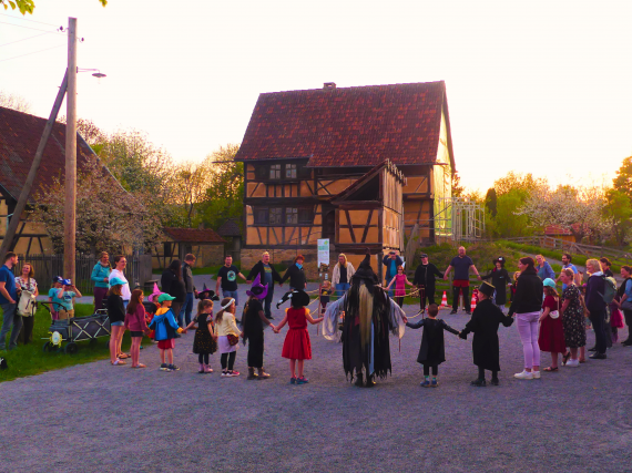 Kinder und Erwachsene stehen vor Fachwerkgeb&auml;ude im Kreis und halten sich an den H&auml;nden