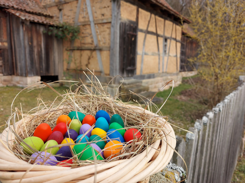 bunte Holzeier im Körbchen auf einem Zaun vor Fachwerkgebäude