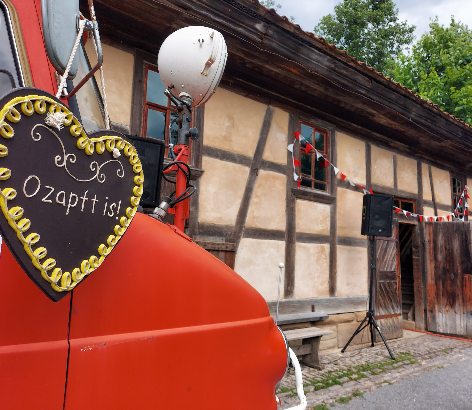 Herz mit Text "O zapft is!" h&auml;ngt an rotem Bus vor Fachwerkgeb&auml;ude