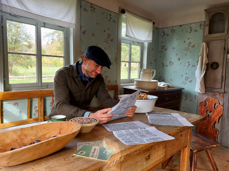 Mann in historischer Kleidung liest Zeitung an einem Holztisch