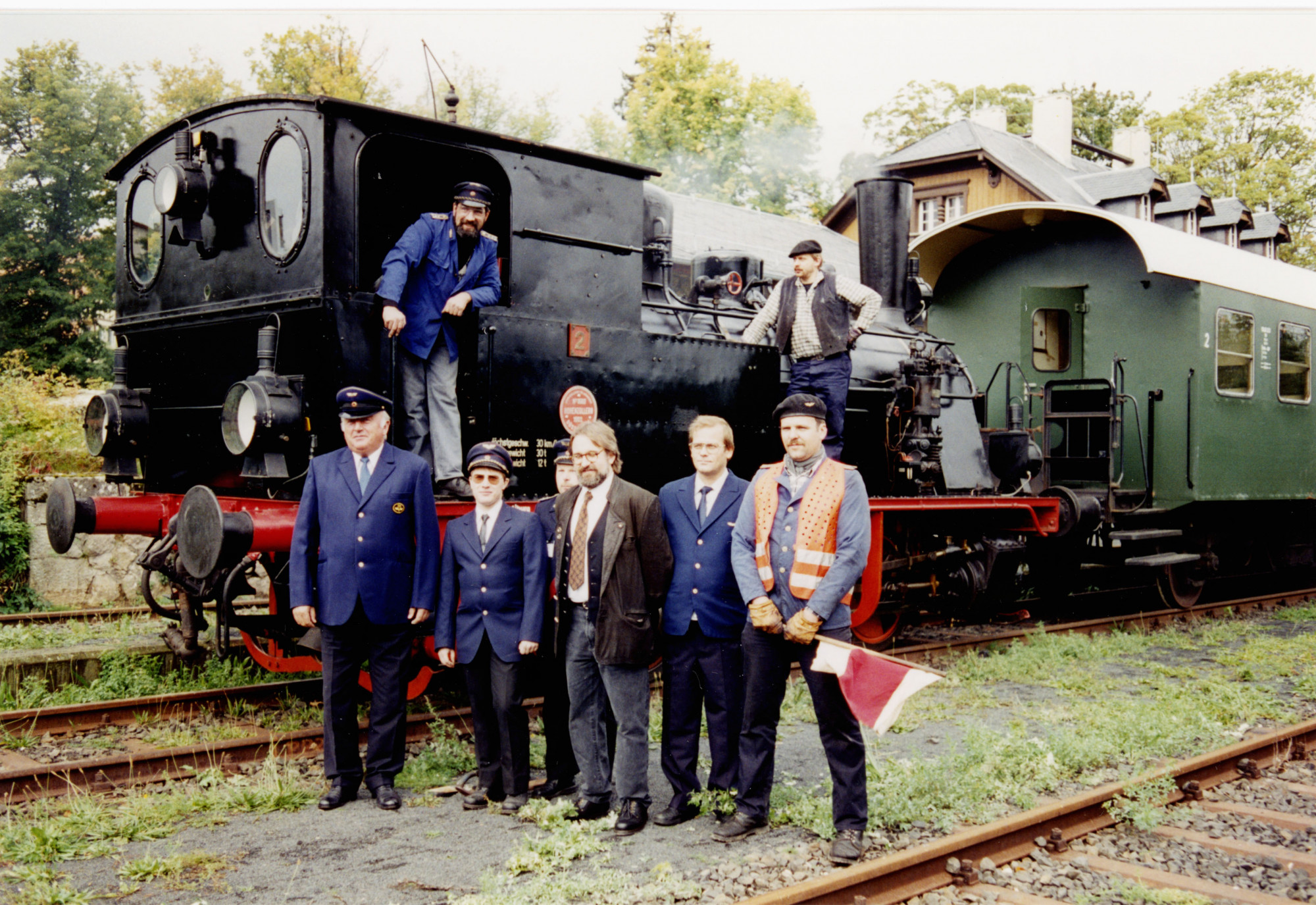 Eine Gruppe von M&auml;nnern steht vor einer Dampflok mit angeh&auml;ngtem gr&uuml;nen Waggon