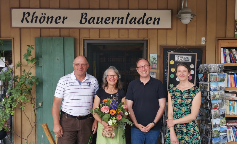 Vier Personen stehen vor dem Eingang des "Rhöner Bauernladen", eine Frau hält einen Blumenstrauß, alle lächeln.